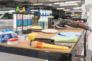 Professional automotive detailer using a paint correction compound and dual-action polisher on a luxury car under LED inspection lights in a detailing studio.