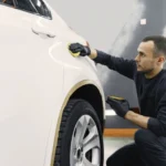 Professional detailer comparing paint correction and paint enhancement on a vehicle under inspection lighting